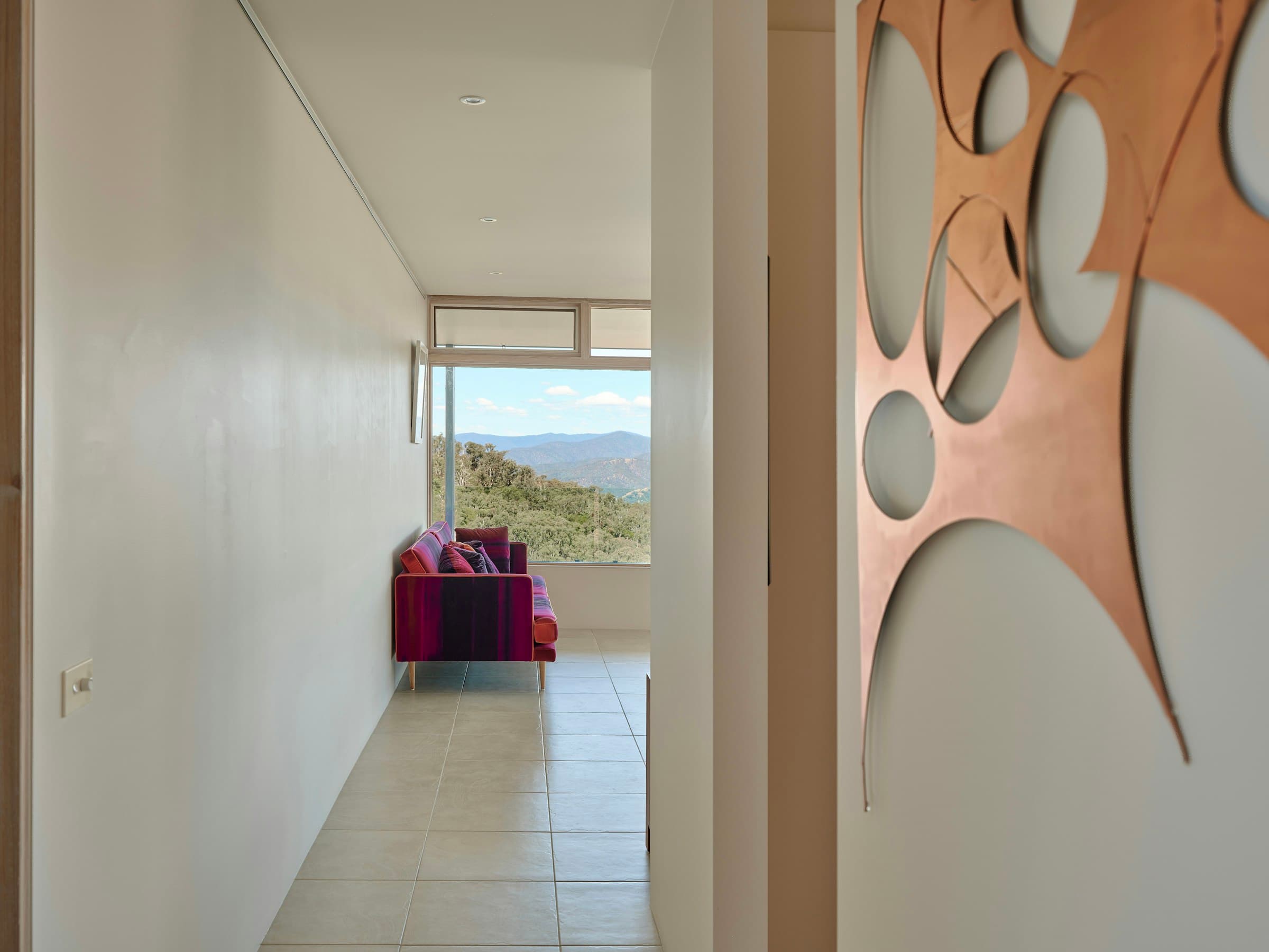 Calm modern Australian residential interior with afternoon light, a deep purple velvet sofa, and a view of mountains through the far window